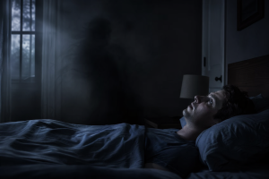 Eine Person liegt wach und reglos in einem dunklen Schlafzimmer, waehrend sich eine schemenhafte unheimliche Praesenz am Bettrand andeutet.